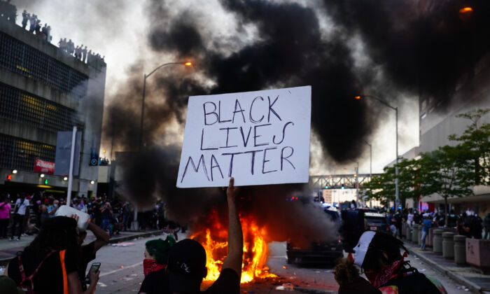 Un hombre sostiene un letrero de Black Lives Matter mientras un coche de policía se incendia delante de él durante una protesta fuera del Centro de CNN en Atlanta, Georgia, el 29 de mayo de 2020. (Elijah Nouvelage/Getty Images)
