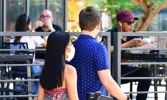 Los paseantes de esta imagen de archivo usan una mascarilla facial mientras otras personas están cenando al aire libre en Los Ángeles, California, el 25 de agosto de 2020. (FREDERIC J. BROWN/AFP vía Getty Images)