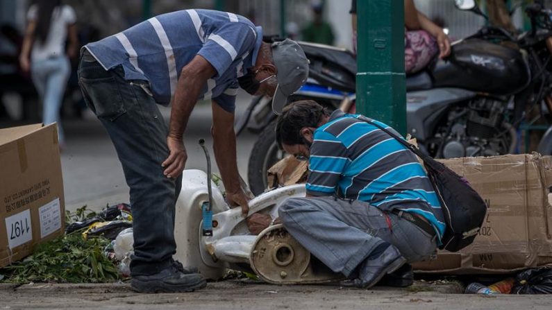Dos hombres desarman una poceta en un basurero el 15 de octubre de 2020, en Caracas (Venezuela). EFE/ Miguel Gutiérrez