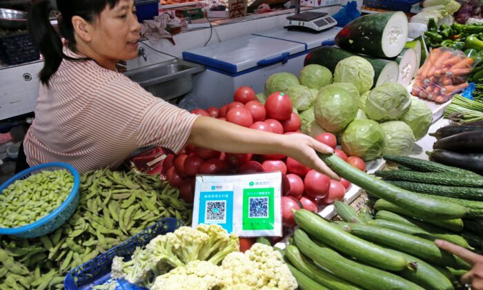 Los códigos QR de Alipay y WeChat para el pago en línea se muestran cuando un proveedor (izq.) entrega verduras a un cliente en un mercado, en la ciudad de Nantong, provincia de Jiangsu, China, el 10 de septiembre de 2018. (STR/AFP a través de Getty Images)