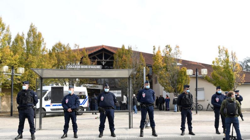 Los policías franceses se ponen de pie cuando los adultos y los niños se reúnen frente a las flores expuestas en la entrada de una escuela secundaria en Conflans-Sainte-Honorine, a 30 km al noroeste de París, el 17 de octubre de 2020, después de que un maestro fuera decapitado por un atacante que había sido muerto a tiros por los policías. (Foto de BERTRAND GUAY / AFP vía Getty Images)
