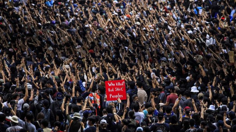 Un manifestante a favor de la democracia (c) muestra un cartel en el que se lee "¿Quién mató a la gente de camisa roja?" mientras que otros saludan con tres dedos durante una protesta contra el gobierno en Bangkok, Tailandia, el 17 de octubre de 2020. EFE/Diego Azubel