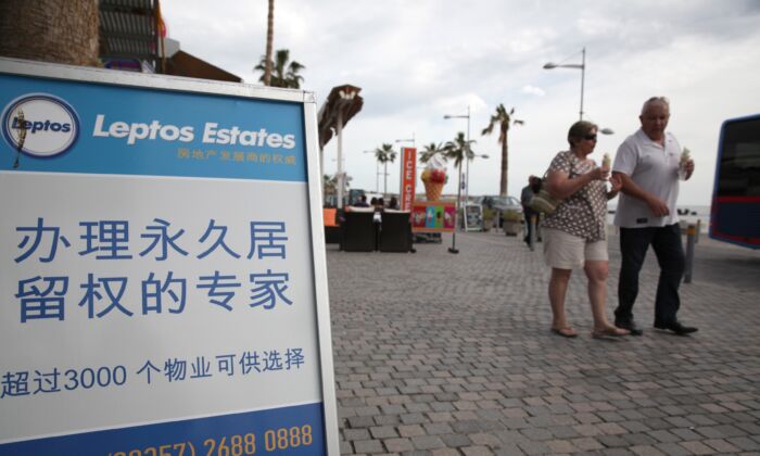 Los turistas pasan por delante de un anuncio de promoción inmobiliaria —dice que comprando un apartamento se puede obtener la condición de residente permanente— en chino en el paseo marítimo del centro turístico chipriota de Paphos el 24 de enero de 2013. (Yiannis Kourtoglou/AFP vía Getty Images)