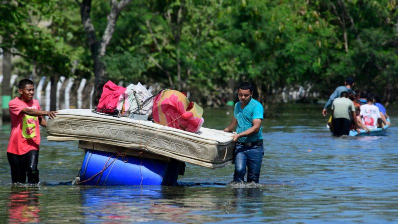 Dos hombres cargan un colchón sobre barriles flotantes en la carretera inundada por la tormenta Eta el 8 de noviembre de 2020 en Río Nance, Honduras. (Foto de Yoseph Amaya / Getty Images)