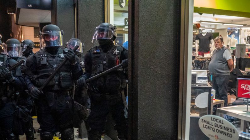Un hombre observa desde el interior de una tienda de ropa mientras la policía de Portland y los agentes del estado de Oregon dispersan a una multitud de manifestantes del black bloc, el 4 de noviembre de 2020, en Portland, Oregon. (Nathan Howard/Getty Images)