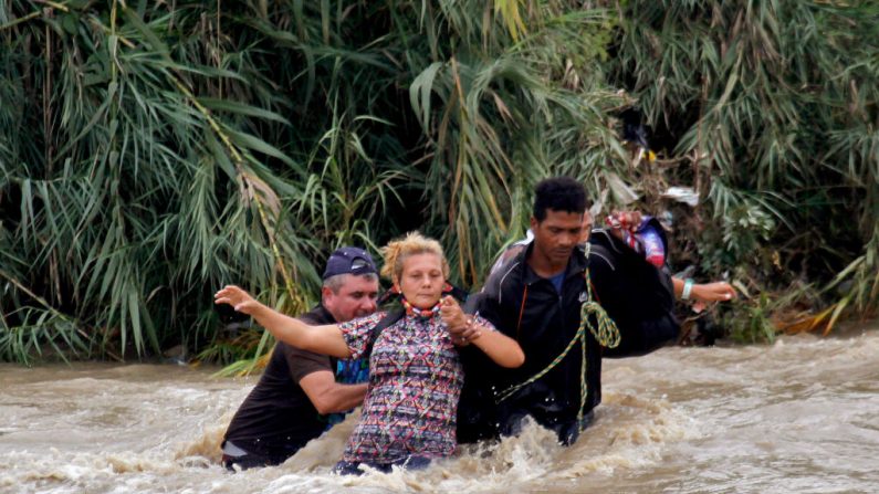 Se ayuda a una mujer a cruzar el río Táchira, la frontera natural entre Colombia y Venezuela, ya que la frontera oficial permanece cerrada debido a la pandemia de COVID-19 en Cúcuta, Colombia, el 19 de noviembre de 2020. Cientos de venezolanos varados en Colombia intentaron cruzar el puente internacional el 18 de noviembre de 2020, ya que las fuertes lluvias habían aumentado el nivel del río. (Foto de SCHNEYDER MENDOZA / AFP a través de Getty Images)