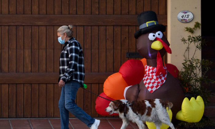 Una mujer con una mascarilla pasea a su perro junto a un pavo inflable antes de las vacaciones del día de Acción de Gracias en medio del aumento de las restricciones de COVID-19 en Manhattan Beach, California, el 21 de noviembre de 2020. (Patrick T. Fallon/AFP a través de Getty Images)