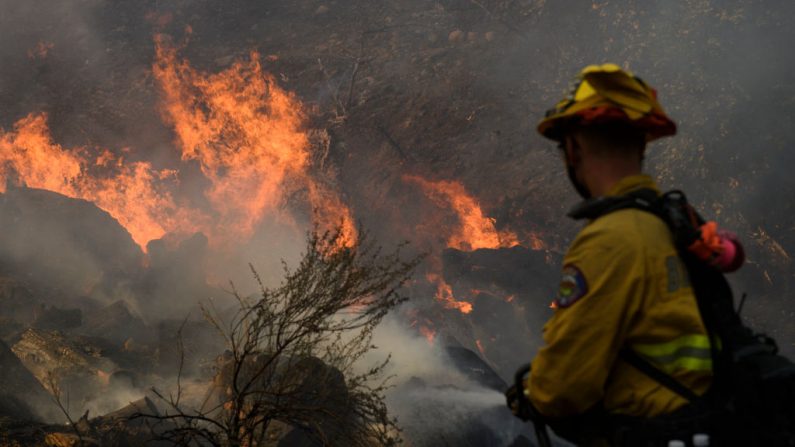 Un bombero de Brea rocía agua para contener el Bond Fire mientras quema los escombros detrás de una estructura cerca de Lake Forest, California (EE.UU.), el 3 de diciembre de 2020. (Foto de PATRICK T.FALLON / AFP vía Getty Imágenes)