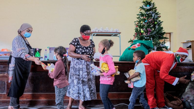 Los voluntarios de la organización benéfica de base Hunger Has No Religion y el personal local de Coronationville Secondary School distribuyen porciones de comida y regalos en Coronationville, Johannesburgo, el 23 de diciembre de 2020. (LUCA SOLA/AFP a través de Getty Images)