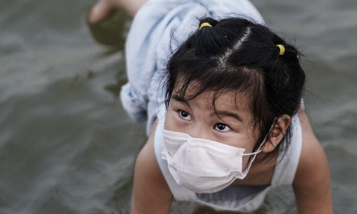 Una niña con una mascarilla juega en un parque de Jiangtan inundado por las fuertes lluvias a lo largo del río Yangtsé el 30 de junio de 2020 en Wuhan, China. Desde el 13 de junio de 2020 el nivel de respuesta a las emergencias de salud pública en la provincia de Hubei se ha reducido al nivel 3. La comisión de salud de Wuhan dijo que la ciudad no tenía casos asintomáticos al 15 de junio, y no hay más contactos cercanos bajo observación médica. (Foto de Getty Images)