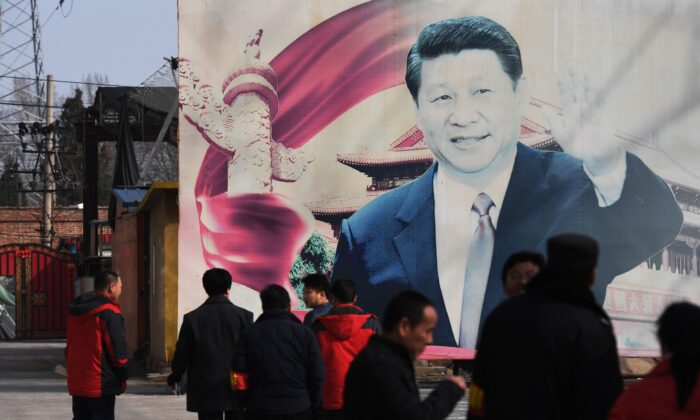 Algunas personas se encuentra de pie cerca de un cartel de propaganda 
 con una imagen del líder chino Xi Jinping, en un aparcamiento de Beijing el 19 de marzo de 2018. (Greg Baker/AFP vía Getty Images)