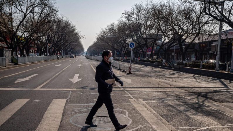 Un hombre con una mascarilla y guantes camina por una calle casi vacía en Beijing el 23 de febrero de 2020. (Nicolas Asfouri/AFP vía Getty Images)
