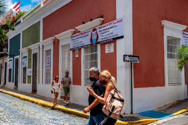 La gente pasa junto a una pancarta instando a los visitantes a usar mascarillas en San Juan, Puerto Rico el 20 de julio de 2020. (Foto de Ricardo Arduengo / AFP vía Getty Images)