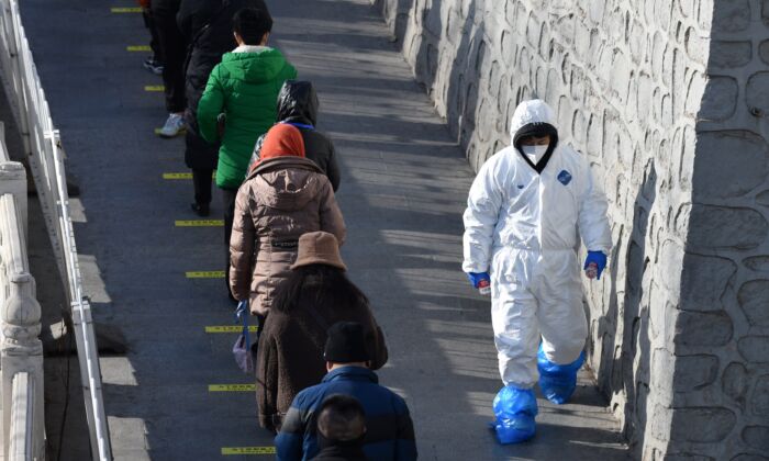 Un trabajador de la salud pasa por delante de los residentes de Beijing que hacen cola para ser examinados para el COVID-19 el 11 de enero de 2021 (GREG BAKER/AFP vía Getty Images)