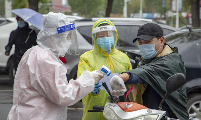 Voluntarios comprueban la temperatura corporal de un residente en la entrada de un complejo residencial en la ciudad de Jilin, China, el 22 de mayo de 2020. (STR/AFP vía Getty Images)