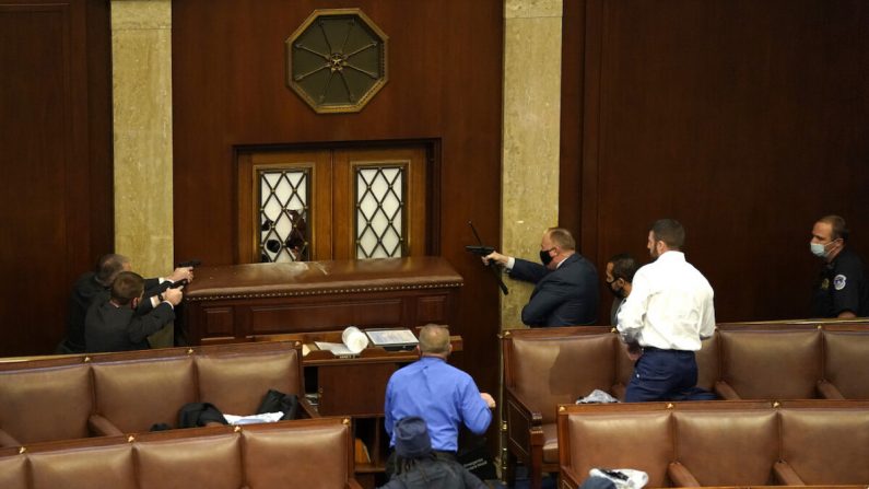 Agentes del orden apuntan con sus armas a una puerta que fue vandalizada en la Cámara durante una sesión conjunta del Congreso en Washington, el 6 de enero de 2021. (Drew Angerer/Getty Images)