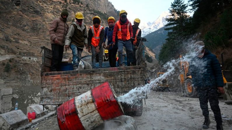 Los trabajadores de la Organización de Carreteras Fronterizas (BRO) descargan barriles de diésel de un camión en una carretera que conduce al destruido puente Raini del distrito de Chamoli (India) el 8 de febrero de 2021 después de que fuera arrastrado por una inundación repentina que se cree que fue causada después de la explosión de un glaciar el 7 de febrero. (Foto de Sajjad Hussain / AFP a través de Getty Images)