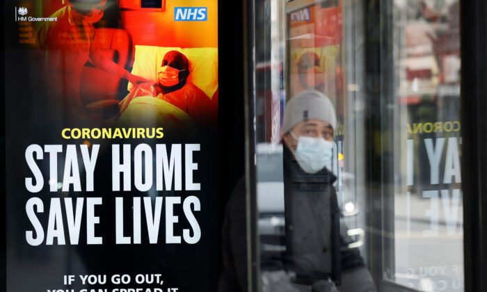 Un viajero lleva una mascarilla mientras se sienta en una marquesina de autobús en el barrio Chinatown del centro de Londres, donde se muestran carteles del Servicio de Salud que promueven: "Quédate en casa, salva vidas".  8 de enero de 2021. (Tolga Akmen /AFP vía Getty Images)