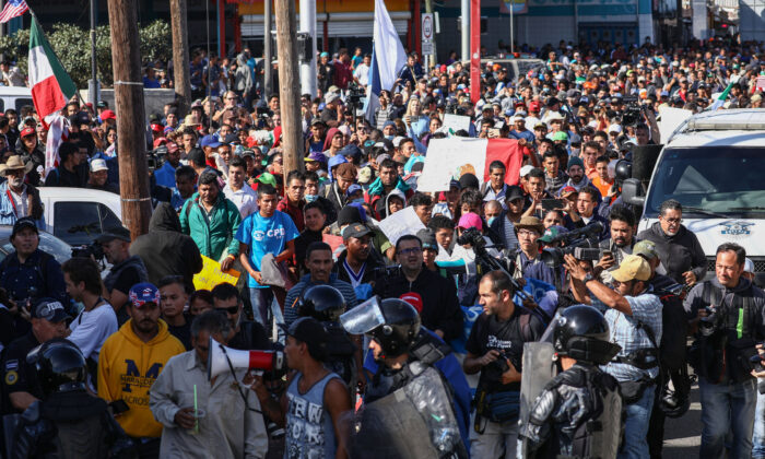 Los migrantes pasan corriendo junto a la policía antidisturbios al pie de un puente que va desde el campamento de migrantes a la entrada peatonal de El Chaparral en el cruce fronterizo de San Ysidro en Tijuana, México, el 25 de noviembre de 2018. (Charlotte Cuthbertson/The Epoch Times)