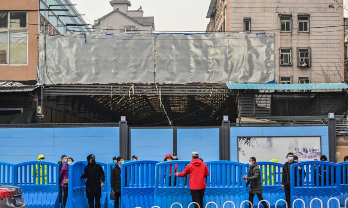 Unos trabajadores colocan barreras fuera del mercado mayorista de mariscos Huanan cerrado durante una visita de miembros del equipo de la Organización Mundial de la Salud (OMS), que investiga los orígenes de la COVID-19 en Wuhan, en la provincia central china de Hubei, el 31 de enero de 2021. (Hector Retamal/AFP vía Getty Images)