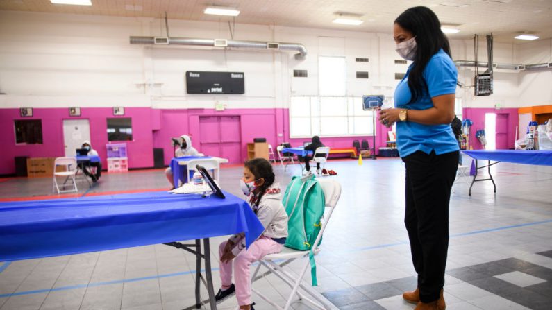 Un miembro del personal de YMCA ayuda a una niña mientras asiste a clases en línea en un centro de aprendizaje dentro de Crenshaw Family YMCA durante la pandemia de covid-19 el 17 de febrero de 2021 en Los Ángeles, California. (Patrick T.Fallon / AFP a través de Getty Images)
