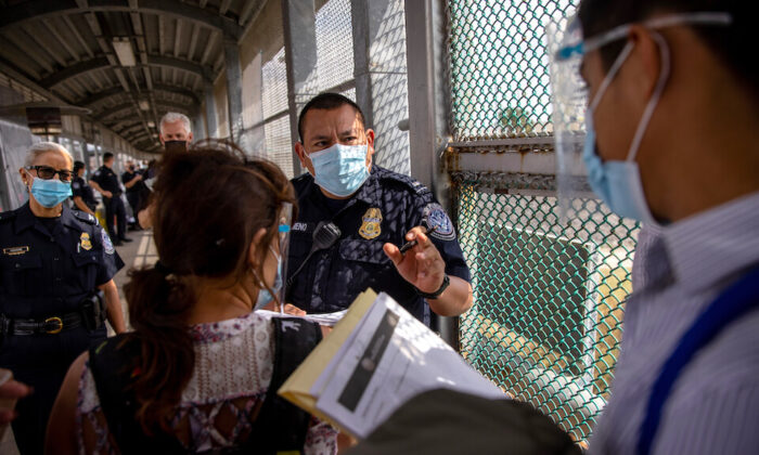 Un oficial de Aduanas y Protección Fronteriza habla con inmigrantes en la frontera entre México y Estados Unidos en Matamoros, México, el 25 de febrero de 2021. (John Moore/Getty Images)