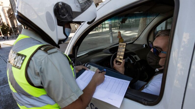 Un policía revisa el teléfono móvil de un conductor en un puesto de control en Santiago, Chile, el 27 de marzo de 2021, durante un encierro en medio de la pandemia de COVID-19. (Martin Bernetti / AFP vía Getty Images)