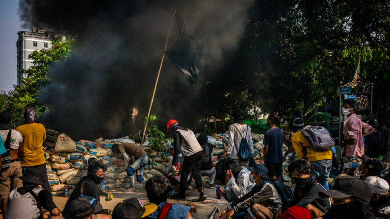 Los manifestantes antigolpistas se preparan para defenderse de las fuerzas de seguridad detrás de una barricada mientras el humo de los neumáticos de automóviles quemados se eleva el 28 de marzo de 2021 en Rangún, Birmania. (Stringer / Getty Images)