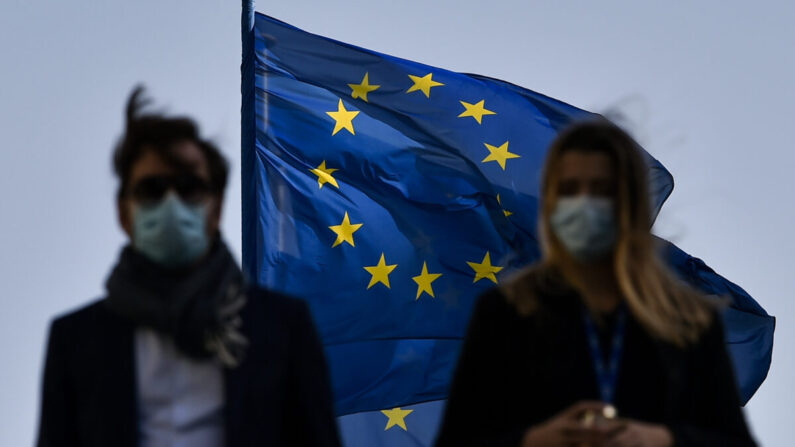 Los peatones caminan frente a la bandera de la Unión Europea en el distrito de la sede de la UE, en Bruselas, el 23 de febrero de 2021. (John Thys/AFP vía Getty Images)