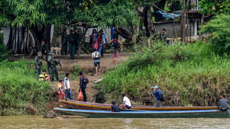 Venezolanos abordan botes para cruzar el río Arauca desde La Victoria, estado de Apure, Venezuela, hasta el municipio de Arauquita, departamento de Arauca, Colombia, cerca de militares venezolanos, el 26 de marzo de 2021. (Daniel Martinez/AFP vía Getty Images)