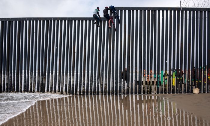 Los migrantes centroamericanos se sientan sobre la valla fronteriza entre Estados Unidos y México mientras un agente de la Patrulla Fronteriza monta guardia, en el estado de Baja California, México, el 21 de marzo de 2019. (Guillermo Arias/AFP/Getty Images)