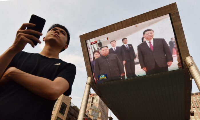 Un hombre espera un taxi fuera de un centro comercial en Beijing, China, el 20 de junio de 2019, mientras detrás se despliegan en una pantalla grande las imágenes del líder chino Xi Jinping (der) mientras es saludado en Pyongyang por el líder norcoreano Kim Jong-un (Greg Baker/AFP vía Getty Images)