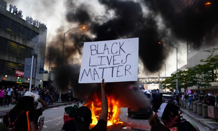 Un hombre sostiene un cartel de Black Lives Matter mientras un coche de policía se quema durante una protesta en Atlanta, Georgia, el 29 de mayo de 2020 (Elijah Nouvelage/Getty Images)