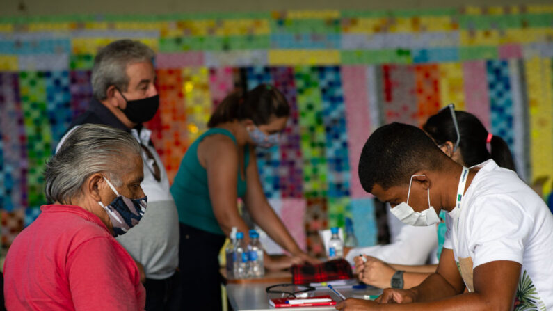 La gente espera una dosis de la vacuna contra el coronavirus (COVID-19) frente al panel en honor a las víctimas fatales de la enfermedad, en el Centro de Saúde 07, el 29 de marzo de 2021, en Brasilia Ceilândia, Brasil. (Andressa Anholete/Getty Images)