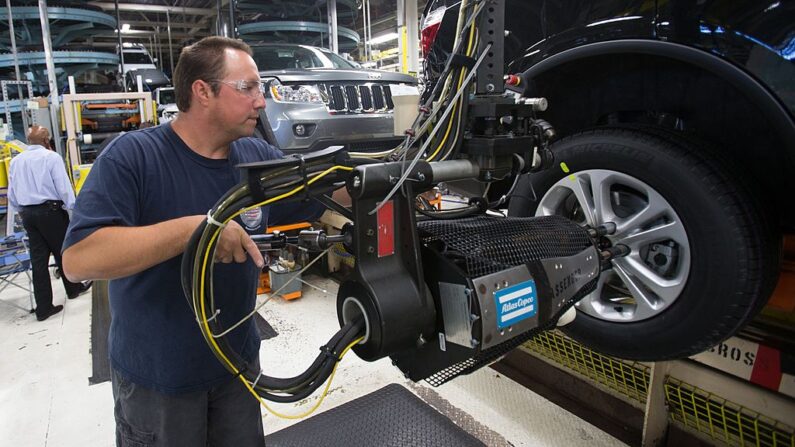 Un trabajador monta los neumáticos en un SUV de Chrysler mientras se mueve a lo largo de la línea de montaje en la planta de ensamblaje Jefferson North en Detroit Michigan, el 7 de agosto de 2012. La planta produce el Jeep Grand Cherokee y el Dodge Durango. (Geoff Robins/AFP vía Getty Images)