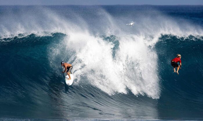Un surfista desliza sobre una ola mientras otro se vuelca hacia el agua en Pipeline, la costa norte de Oahu, Hawái, el 14 de febrero de 2021. (Brian Bielmann/AFP vía Getty Images)