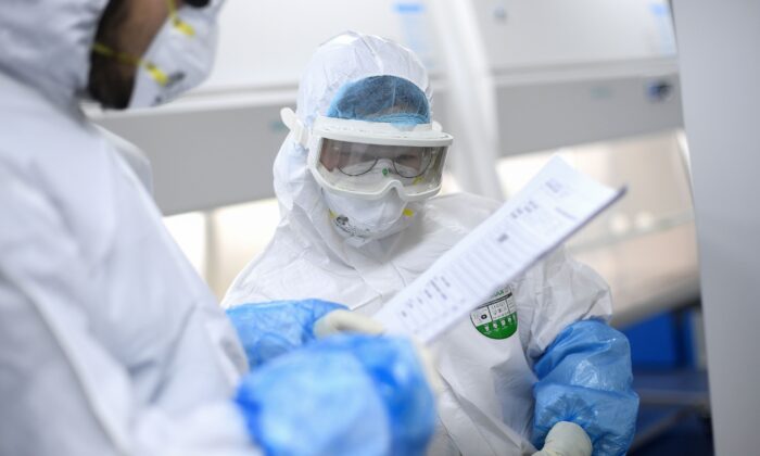 Unos técnicos de laboratorio hablan mientras trabajan en las muestras que serán analizadas para detectar COVID-19, en un laboratorio BGI, en Wuhan, China, el 6 de febrero de 2020. (STR/AFP vía Getty Images)