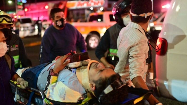 Trabajadores de emergencia llevan a una persona herida en una camilla después de que un paso elevado para un metro se derrumbó parcialmente en la Ciudad de México el 3 de mayo de 2021. (PEDRO PARDO/AFP via Getty Images)