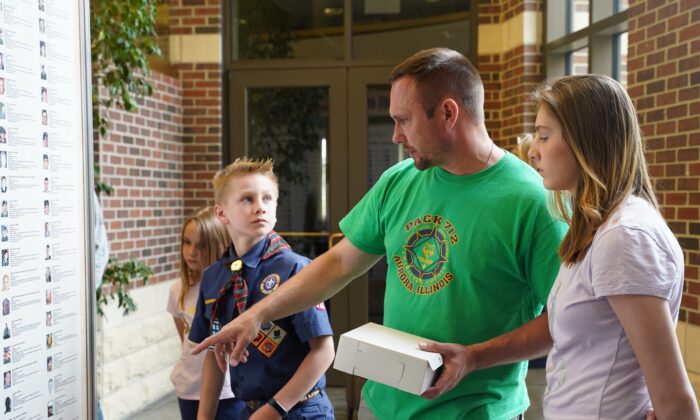 Drew Barczak le habla a sus hijos sobre los soldados caídos en el Muro de Honor expuesto en la alcaldía de Oswego, Illinois, el 31 de mayo de 2021. (Cara Ding/The Epoch Times)