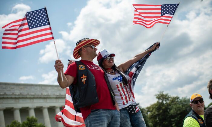 Una pareja que agita banderas de Estados Unidos mira mientras unos motociclistas participan en el desfile "Rolling Thunder", que forma parte del fin de semana conmemorativo en honor a los veteranos de guerra en Washington, el 26 de mayo de 2019. (Eric Baradat /AFP vía Getty Images)
