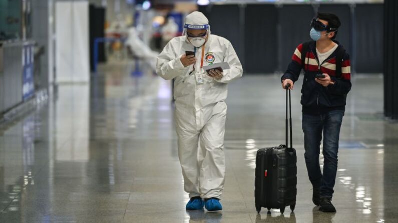 Un miembro de la seguridad aeroportuaria, con equipo de protección contra el brote de coronavirus COVID-19, camina con un pasajero a su llegada al aeropuerto internacional de Shanghai Pudong, en Shanghai, el 26 de marzo de 2020. (Foto de HECTOR RETAMAL/AFP a través de Getty Images)