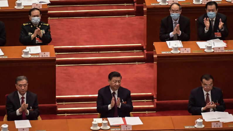 Wang Yang (i), miembro del Comité Permanente del Politburó, el mandatario chino Xi Jinping (c) y el primer ministro Li Keqiang aplauden después de que se anunciara el resultado de la votación sobre los cambios en el sistema electoral de Hong Kong durante la sesión de clausura de la Asamblea Nacional Popular (ANP) en el Gran Salón del Pueblo en Beijing, el 11 de marzo de 2021. (Nicolas Asfouri/AFP vía Getty Images)