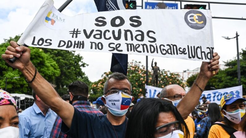 Un activista de la oposición con máscaras para evitar la propagación del COVID-19 sostiene una pancarta durante una protesta para exigir al régimen la vacunación general de la población en Caracas (Venezuela) el 28 de mayo de 2021. (Yuri Cortez / AFP vía Getty Images)