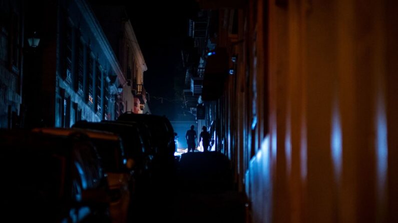 Personas caminando en una calle que quedó a oscuras por un corte de energía debido a un ciberataque en el Viejo San Juan, Puerto Rico, el 10 de junio de 2021. (Ricardo Arduengo / AFP vía Getty Images)