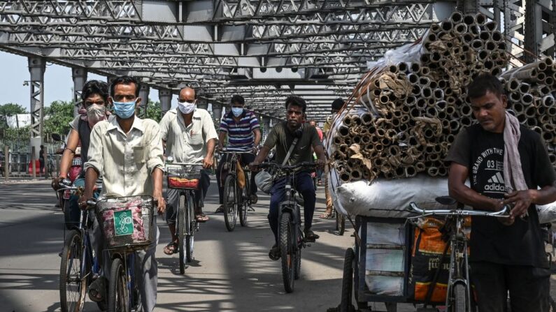 Los transeúntes cruzan el puente de Howrah en sus bicicletas mientras el gobierno estatal suspende el transporte público regular durante el bloqueo impuesto para frenar la propagación del covid-19, en Calcuta (India) el 23 de junio de 2021. (Dibyangshu Sarkar / AFP vía Getty Images)