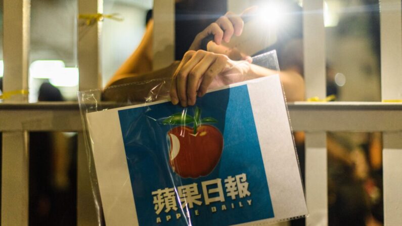 Un simpatizante sostiene un cartel con el logotipo del periódico Apple Daily frente al edificio de oficinas de la compañía de medios de comunicación en Hong Kong en las primeras horas del 24 de junio de 2021. (Anthony Wallace/AFP vía Getty Images)