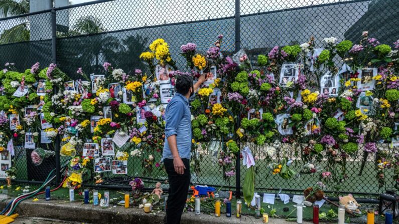 Un hombre agrega flores a un monumento con fotos de algunos de los que se perdieron en el edificio Champlain Towers South de 12 pisos parcialmente derrumbado el 28 de junio de 2021 en Surfside, Florida. (Giorgio VIERA/AFP a través de Getty Images)