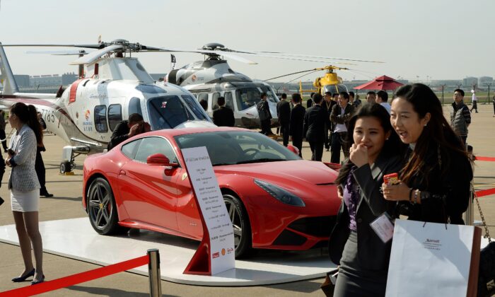 Un grupo de personas que pasa por delante de un coche Ferrari y de los helicópteros que varias multinacionales comercializan a los chinos ricos durante la Conferencia y Exposición de Aviación de Negocios de Asia (ABACE2014) en el aeropuerto de Shanghai Hongqiao el 14 de abril de 2014. (MARK RALSTON/AFP vía Getty Images)