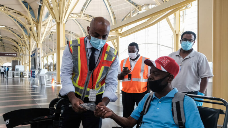 Un empleado de la aerolínea Delta da una mascarilla a un pasajero durante la facturación en el Aeropuerto Nacional Ronald Reagan en Arlington, Virginia, el 22 de julio de 2020. (Michael A. McCoy/Getty Images)