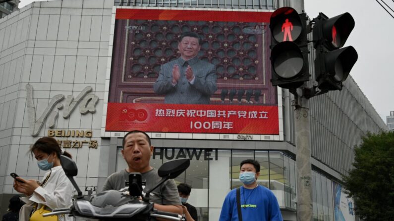 La gente camina frente a una gran pantalla que muestra al líder chino Xi Jinping dando un discurso durante las celebraciones para conmemorar el centenario de la fundación del Partido Comunista Chino en Beijing el 1 de julio de 2021. (Noel Celis/AFP vía Getty Images)